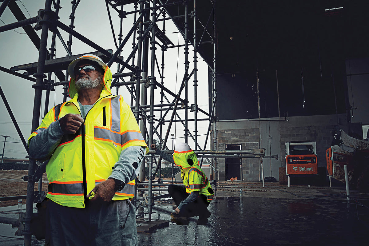 Construction workers in high-visibility vests working near scaffolding on a job site.