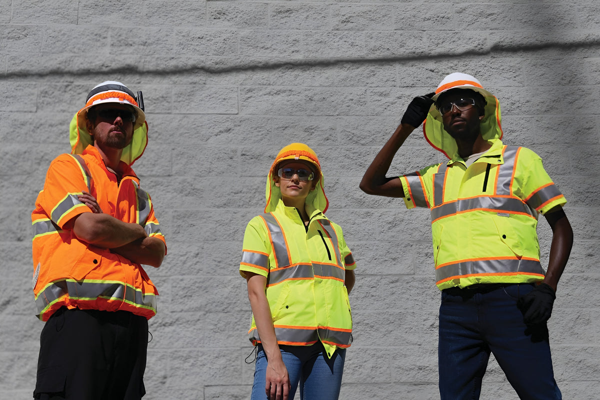 Three construction workers in high-visibility safety gear and hard hats standing in front of a gray brick wall.