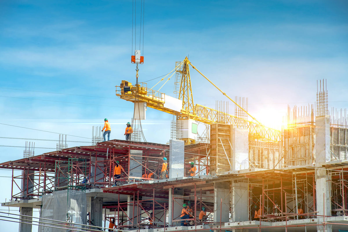 Construction workers and a yellow crane on a building site under a blue sky.